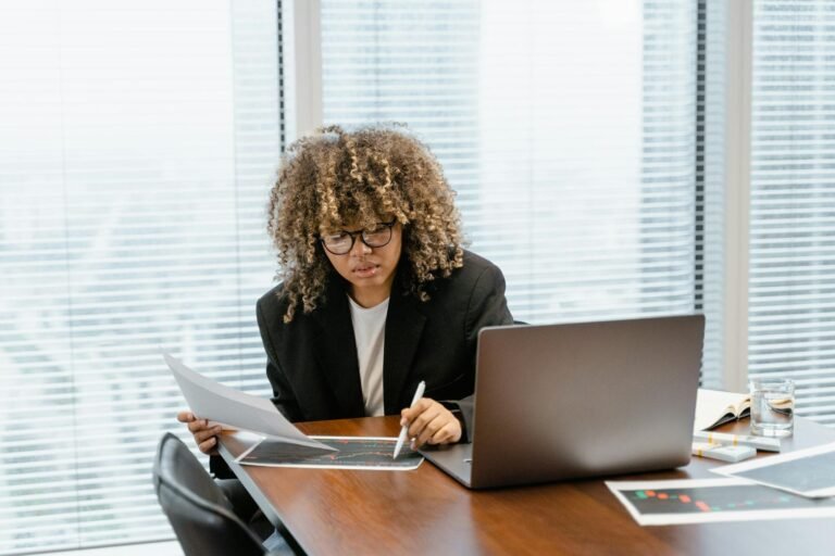 A young professional analyzing financial charts at a modern office desk with a laptop.